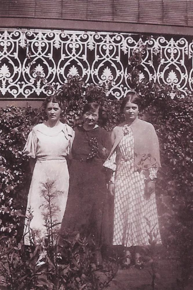 Three women standing in front of a verandah in 1935. The two younger women have a box round their faces; the woman in the middle does not.